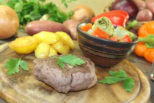 Ostrich steak with crispy baked potatoes and vegetables on a wooden board