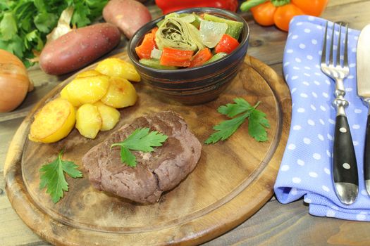 roasted ostrich steaks with baked potatoes and parsley on a wooden board