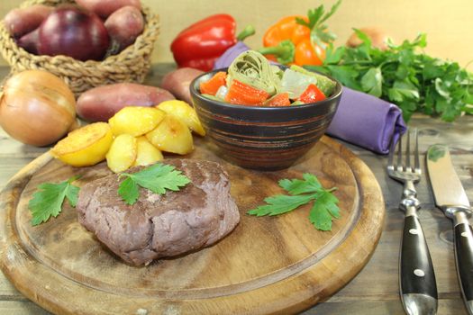 Ostrich steak with crispy baked potatoes and parsley on a wooden board