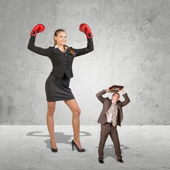 Successful businesswoman flexing her powers in a conceptual image of a giant business woman wearing boxing gloves towering over a cowering businessman sheltering under his briefcase