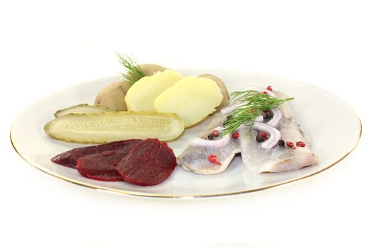 a plate of pickled herring fillet, boiled potatoes, beetroot and pickled gherkins