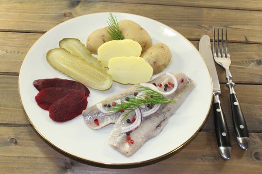 a plate of pickled herring fillet, boiled potatoes, beetroot and pickled gherkins