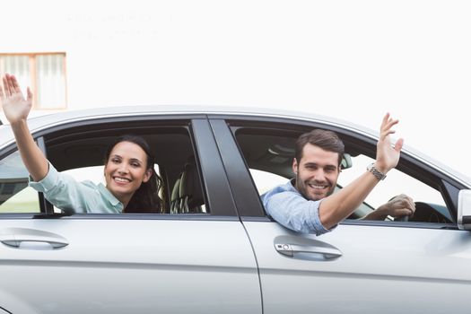 Young couple smiling and waving in their car