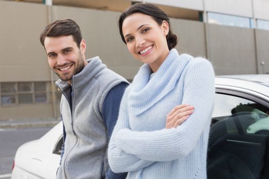 Young couple smiling at the camera outside their car