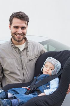 Father carrying baby in his car seat smiling at camera