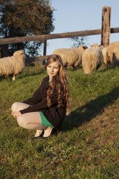 Young long-haired curly blonde woman in a corral with sheeps
