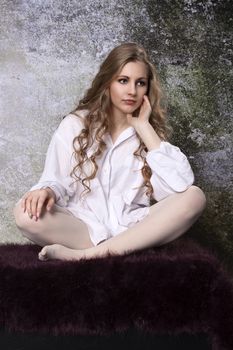 Young long-haired curly blonde woman on the sofa with a hairy blanket in front of an old dilapidated wall