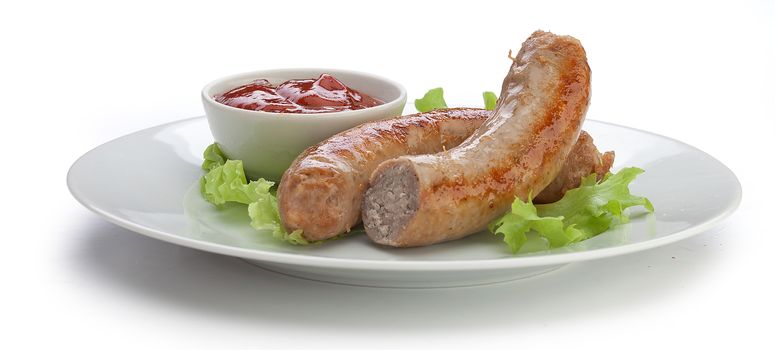 Two roasted sausages with fresh green lettuce and red tomato sauce on the white plate