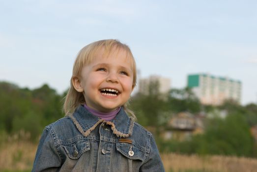 The little girl laughs at a green lawn.