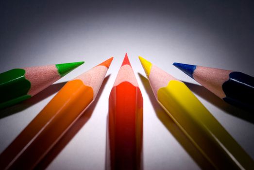 Five pencils (dark blue, green, red, yellow, orange) on a dark background.