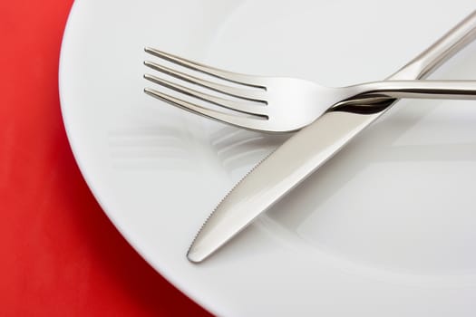 White empty plate with fork and knife on red