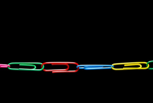 Color office paper clips on a black background.