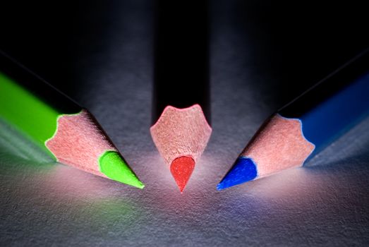 Three pencils (dark blue, green, red) on a dark background.