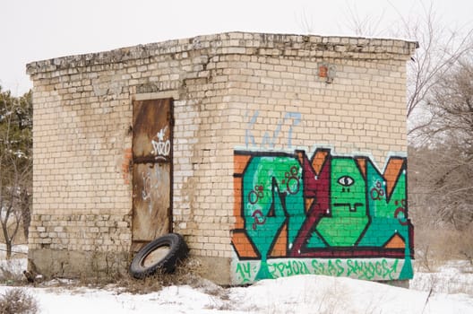 An old one-story brick building with a rusty door with graffiti on the wall
