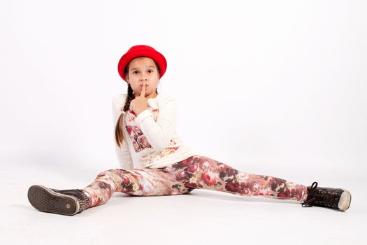 Girl sitting on the floor, legs astride, in a red hat