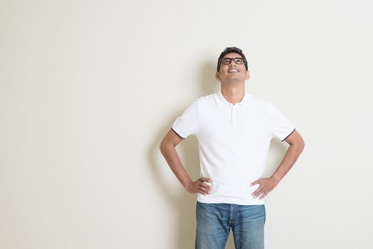 Portrait of handsome Indian guy looking up, standing on plain background with shadow, copy space at side.