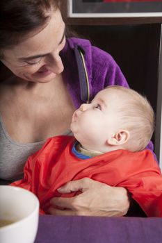 six months age blonde caucasian baby red bib in woman mother purple velvet jacket arms eating puree