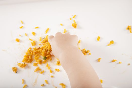 overhead shot of one year age caucasian baby hand taking yellow rice on white table