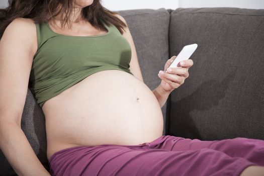 pregnant woman reading smartphone sitting in sofa