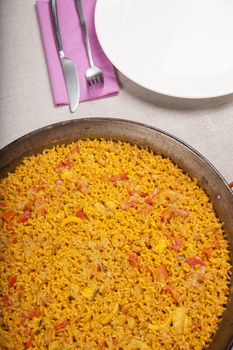 spanish paella in paellera pan next to white dish