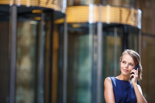 Gorgeous young businesswoman calling on her phone in front of her company's building (shallow DOF; color toned image)