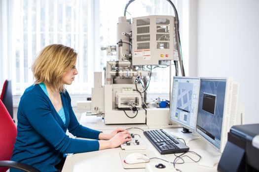 Pretty, female researcher using a microscope in a lab, doing research (color toned image)