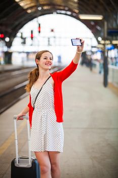 Pretty young woman at a train station - taking a selfie with her smart phone