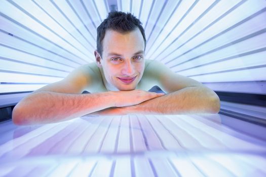 Handsome young man relaxing during a tanning session in a modern solarium, taking care of himself, enjoying the artificial sunlight.