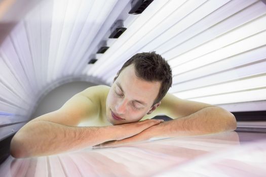 Handsome young man relaxing during a tanning session in a modern solarium, taking care of himself, enjoying the artificial sunlight.