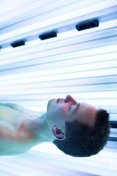 Handsome young man relaxing during a tanning session in a modern solarium, taking care of himself, enjoying the artificial sunlight.