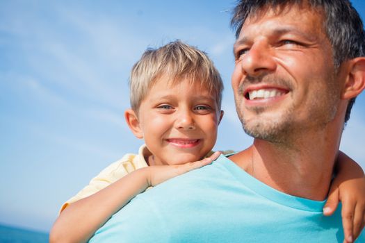 Closeup portrait og father holding son on his shoulders at the beach