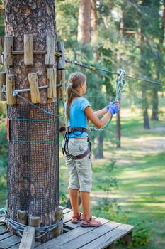 Happy school girl enjoying activity in a climbing adventure park on a summer day