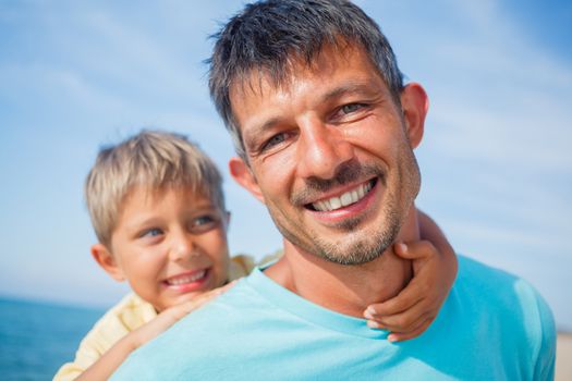 Closeup portrait og father holding son on his shoulders at the beach