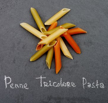 Heap of Raw Penne Triciolore Pasta with Inscription closeup on Black Stone background