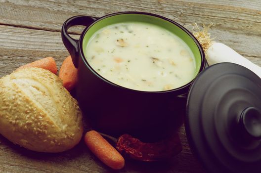 Healthy Vegetable Creamy Soup with Raw Ingredients and Sesame Bun in Pannikin closeup on Rustic Wooden background. Retro Styled