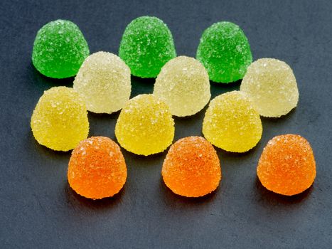 Arrangement of Multi Colored Jelly Fruit Candy closeup on Black Stone background. Focus on Foreground