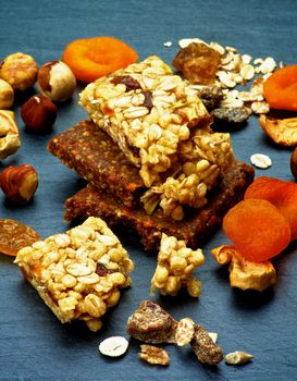 Stack of Useful Granola Bars with Muesli, Nuts, Seed, Raisins and Dried Apricots closeup on Black Stone background