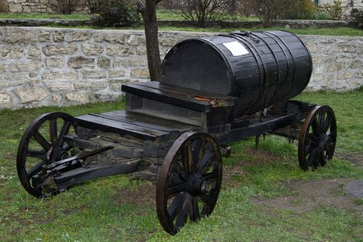 Old wooden barrel on cart. Vintage black barrel wagon transports water.