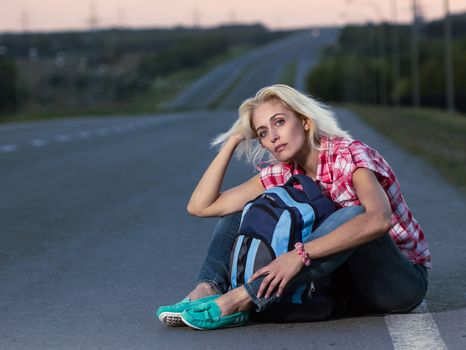 Hitch-hiking: woman with haversack sitting on the road
