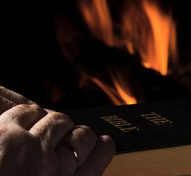 Hands of a man with a Bible on fire background