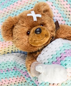 Sick teddy bear with bandage in a bed