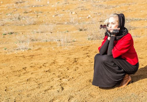 Beautiful blonde woman sitting on the sand, spring day