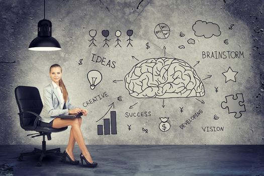 Young Businesswoman Sitting in Office Chair Underneath Overhead Light next to Wall Covered in Idea Themed Illustrations, in Brainstorming Concept Image