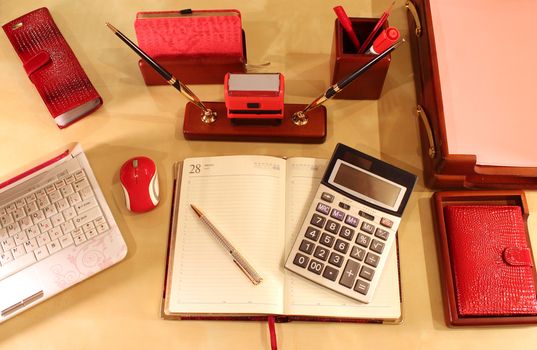 Open diary, calculator, computer, mobile phone, business card, document folders and stationery in red color scheme