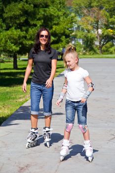 Learning mother and daughter on roller skates in summer