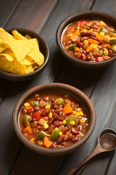 Two rustic bowls of vegetarian chili dish made with kidney bean, carrot, zucchini, bell pepper, sweet corn, tomato, onion, garlic, with tortilla chips on the side, photographed with natural light (Selective Focus, Focus in the middle of the first dish)   