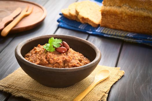 Rustic bowl of homemade red kidney bean spread garnished with kidney beans and fresh coriander leaf, wholegrain bread in the back, photographed with natural light (Selective Focus, Focus on the leaf) 