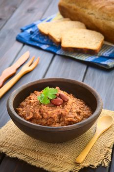 Rustic bowl of homemade red kidney bean spread garnished with kidney beans and fresh coriander leaf, wholegrain bread in the back, photographed with natural light (Selective Focus, Focus on the leaf) 