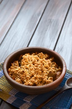 Rustic bowl of baked apple crumble or crisp on kitchen towel, wooden spoon on the side, photographed on dark wood with natural light (Selective Focus, Focus one third into the first crumble)