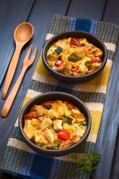 Savory baked vegetarian bread pudding made of zucchini, bell pepper, tomato and diced baguette, seasoned with thyme and parsley in rustic bowl on kitchen towel, photographed on dark wood with natural light (Selective Focus, Focus in the middle of the first dish)